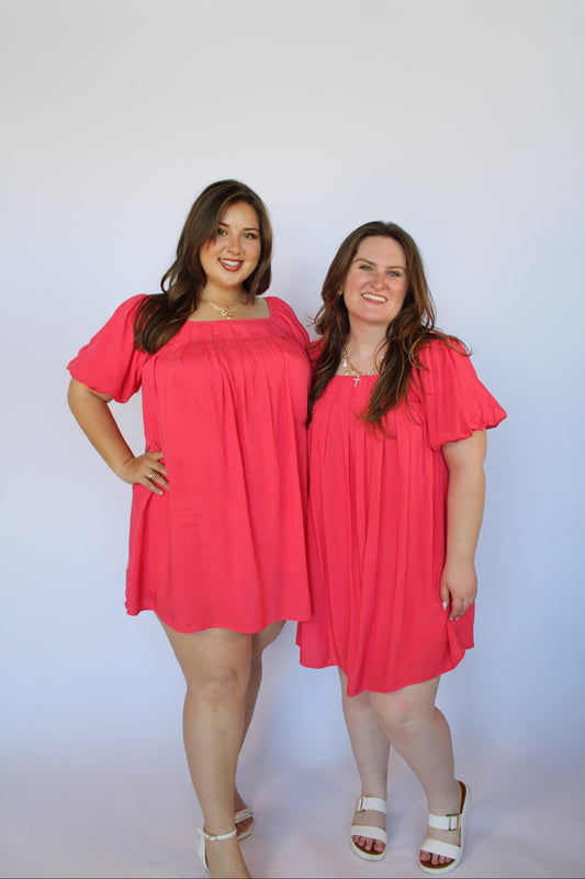 Two women wearing pink dresses against a white background
