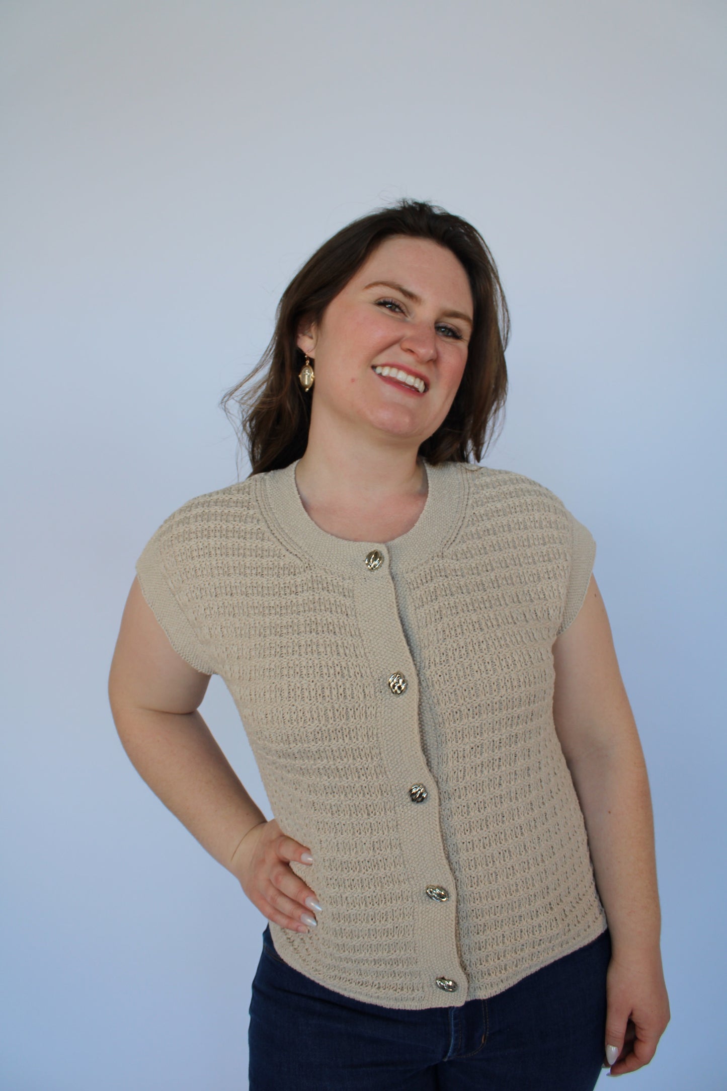 Woman wearing a beige knitted vest against a plain background