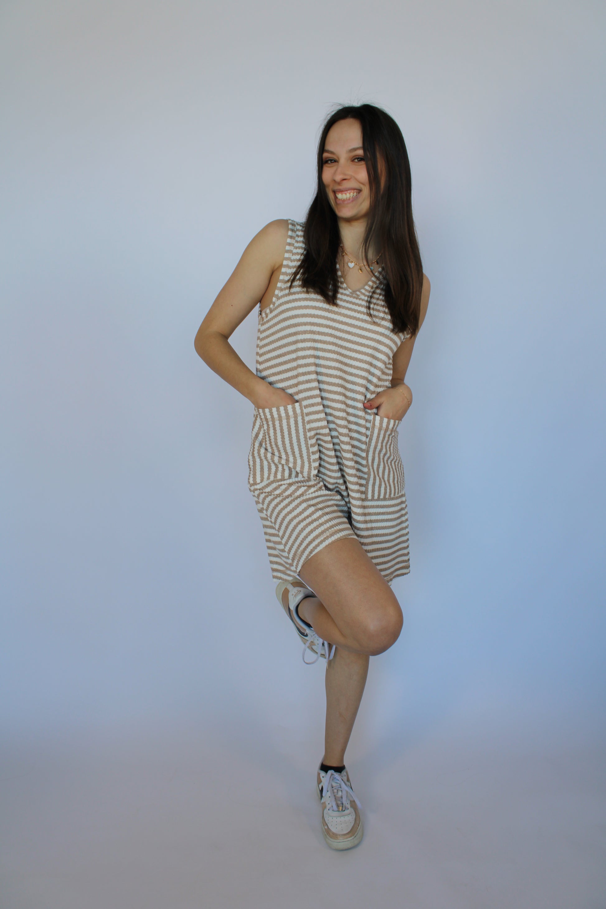 Woman wearing a striped dress and sneakers on a plain background
